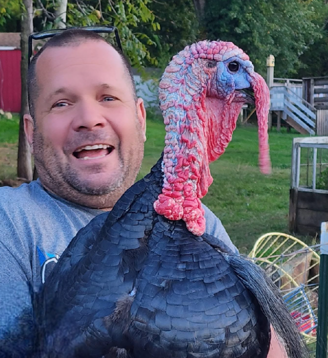 Jeff smiling outdoors with a large turkey in his arms.