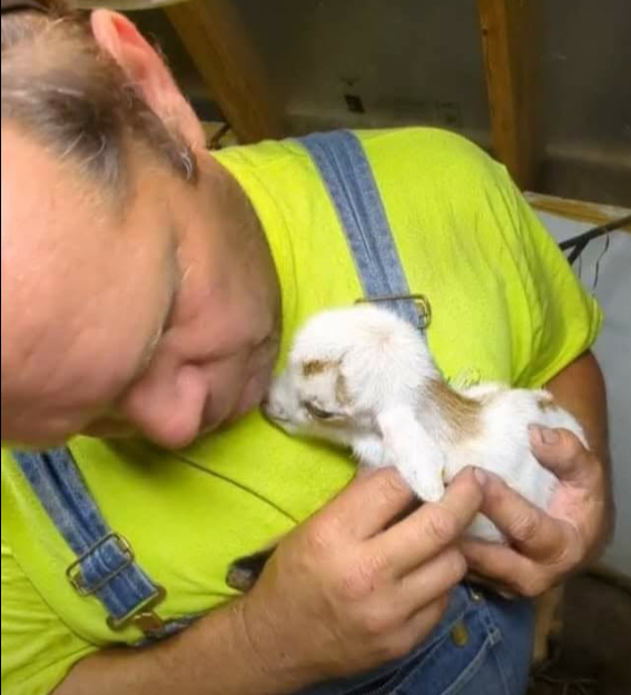 Jeff gently cuddling a tiny white-and-brown goat close to his face.